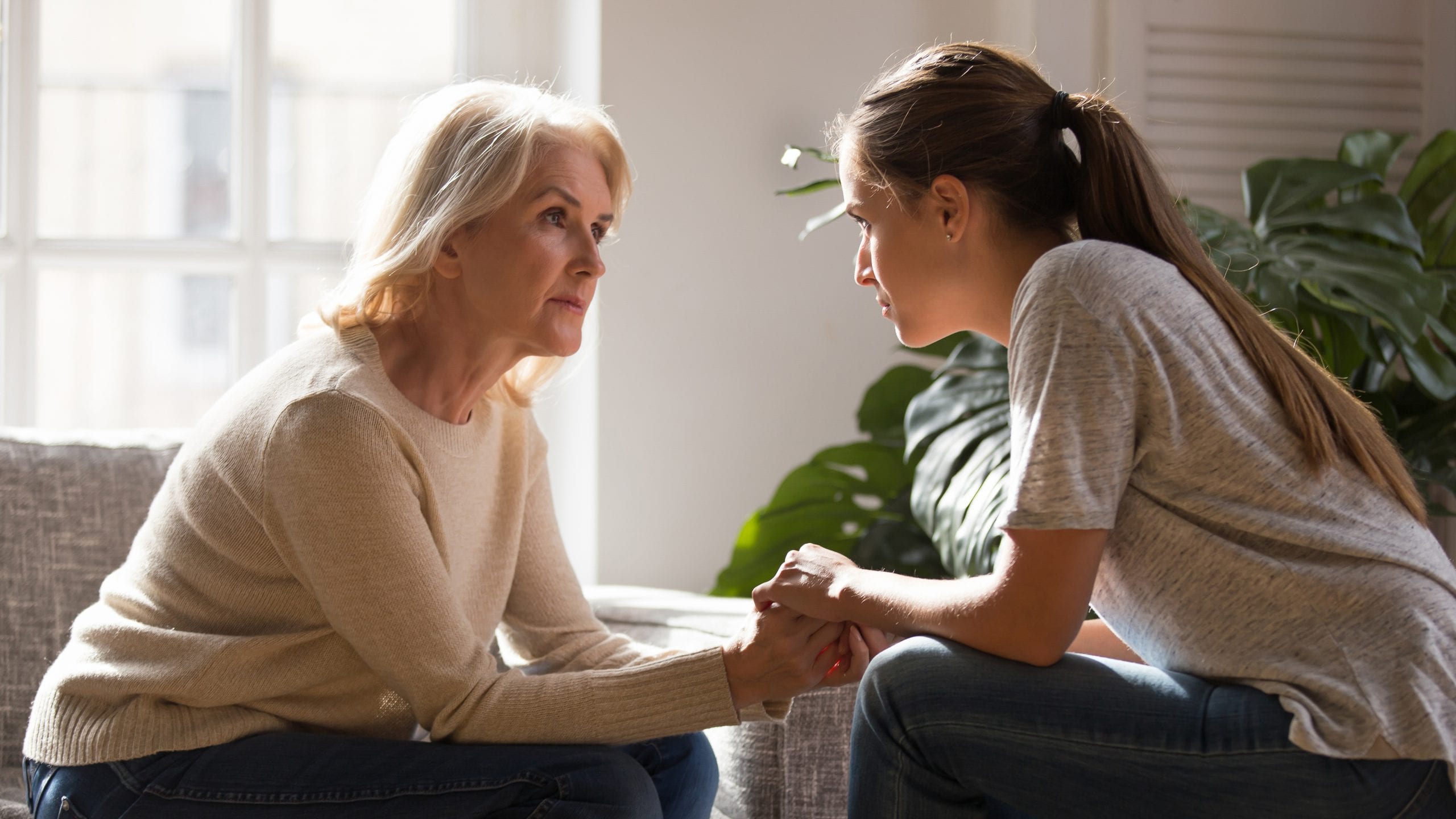 Different generations women talking holding hands giving psychological support Grown up daughter holding hands of middle aged mother relatives female sitting look at each other having heart-to-heart talk, understanding support care and love of diverse generations women concept